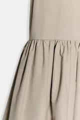 Vestido midi sin mangas de cuello redondo, con falda amplia con frunces y bolsillos laterales ocultos. Presenta cierre en la espalda con abertura y botón.