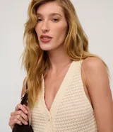 Chaleco de punto color beige claro, con cuello en V y cierre frontal de botones. El tejido presenta un patrón texturizado de pequeños puntos.