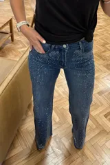 Jeans de denim azul con corte ajustado, cintura media y detalles de strass plateados en la parte superior y los laterales.