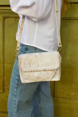 Cartera bandolera de cuero color blanco envejecido con pespuntes marrones. Tiene correa larga regulable y herrajes metálicos color bronce.