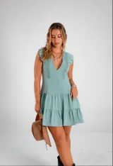 Vestido corto color verde agua, con escote en V profundo, volados en los hombros y detalle de encaje vertical en el frente. Presenta una falda con cortes horizontales que le otorgan movimiento.