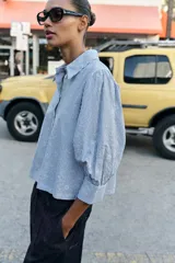 Camisa de cuello solapa y manga larga con puños abotonados. Presenta un diseño de rayas verticales azules y blancas con un estampado floral lineal superpuesto. Cierre frontal con botones.