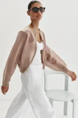 Chaqueta estilo bomber de punto color beige con acabado brillante, cuello redondo, manga larga con puños elásticos y cierre frontal con cremallera.