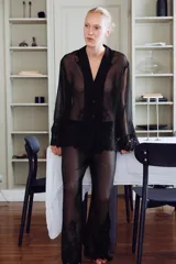 Blusa semitransparente negra de cuello solapa y manga larga, con cierre frontal de botones y detalles de bordados tonales en el ruedo y los puños.