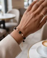 Pulsera de acero con baño de oro, adornada con cuentas cuadradas negras y pequeñas perlas blancas dispuestas alternadamente sobre una cadena eslabonada.