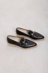 Mocasines negros de cuero con textura símil cocodrilo, punta fina y detalle de herraje metálico dorado en el empeine. Poseen suela plana con borde en tono claro.