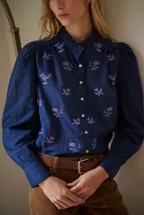 Camisa blanca de manga corta con cuello mao y volados, botones frontales y bordados de hojas y flores en color dorado.