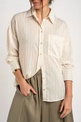 Camisa de manga larga con patrón de rayas sutiles, corte holgado, cuello camisero, cierre frontal con botones y un bolsillo aplicado en el pecho.