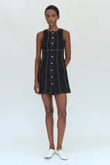 Vestido mini negro con cuello redondo y diseño sin mangas, con pespuntes en contraste y botones decorativos frontales.