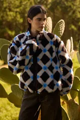 Campera de textura tipo corderito con diseño a cuadros en tonos marrones, negros y beige. Presenta cuello alto, cierre frontal completo y detalles en tela técnica lisa en los laterales y bordes. Posee un elástico ajustable en la parte inferior para regular el calce.