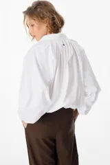 Camisa de corte holgado color marrón chocolate, con cuello clásico, cierre frontal de botones y mangas largas abullonadas con frunces en los hombros.