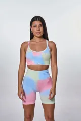 Conjunto deportivo compuesto por un top de escote redondo con breteles finos y un short ciclista de tiro alto. Ambas piezas presentan un diseño estampado estilo tie-dye en tonos pastel de azul, rosa y verde, con el logo de la marca estampado en el frente del top.