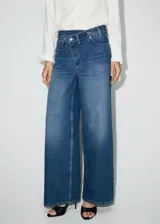Jeans de tiro medio con diseño wide leg, cintura cruzada y cierre frontal asimétrico con cremallera y botones. Cuenta con cinco bolsillos y presillas para cinto.