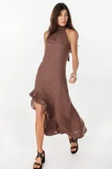 Vestido midi marrón de lino italiano, con cuello halter, sin mangas y diseño asimétrico con volados en el ruedo.