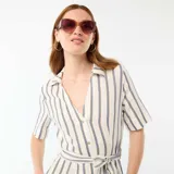 Vestido camisero largo de manga corta en mezcla de algodón y lino, con diseño de rayas verticales en tonos marrón, azul y blanco. Cuenta con cuello en V, cierre frontal abotonado y un lazo ajustable para atar en la cintura.