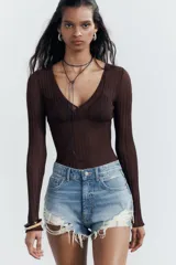 Short de jean negro desgastado, tiro alto, con roturas pronunciadas y terminación deshilachada en el bajo. Presenta cinco bolsillos y cierre frontal con botón metálico.