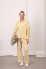 Conjunto de dos piezas compuesto por camisa de manga larga con cuello camisero y botones frontales, y pantalón de corte recto con cintura elástica. Presenta un estampado geométrico de pequeñas flores amarillas sobre fondo blanco.