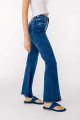 Jean azul claro de corte flare con aberturas en los tobillos y detalles rotos en las rodillas y muslos.