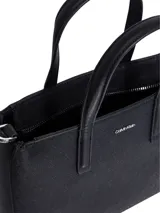 Cartera tipo tote de Calvin Klein, color negro, con doble asa de mano y correa ajustable y extraíble. El cuerpo del bolso presenta un monograma texturizado en relieve.