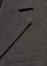Chaqueta de corte recto estilo sastre, color gris, con cuello de solapa con muesca, cierre frontal de tres botones, bolsillos laterales de ribete y un bolsillo de ribete en el pecho. Cuenta con forro interior y mangas largas.