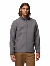 Chaqueta Columbia modelo Ascender Soft Shell, color gris, con cierre frontal completo, cuello alto con protector de barbilla, bolsillo en el pecho con cierre y bolsillos laterales. Cuenta con puños ajustables y tecnología resistente al agua y al viento.