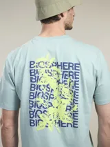 Remera de algodón color verde menta, manga corta y cuello redondo. Estampado grande en la espalda con la palabra "BIOSPHERE" repetida en azul marino y un diseño gráfico de una flor/hojas en amarillo flúor.