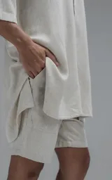Camisa de corte oversize con cuello camisero, cierre frontal de botones y mangas cortas. Presenta un diseño holgado con bolsillos laterales integrados en la costura.