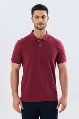 Remera polo lisa de piqué en color bordó, con cuello camisero, cierre frontal con botones y mangas cortas.