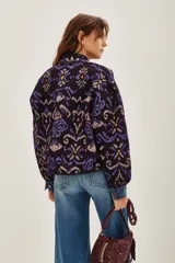Campera bomber acolchada con estampado geométrico en tonos violeta, azul y negro. Presenta cierre frontal con botones a presión, cuello redondo y puños elásticos.