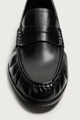 Mocasín de vestir negro de estilo clásico con detalle de antifaz en la parte superior, suela a tono y ligero tacón.