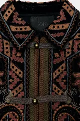 Chaqueta de terciopelo negro con cuello solapa y manga larga. Presenta un diseño con bordados florales y geométricos a contraste en tonos tierra y ocres. Cuenta con cierre frontal de botones y forro interior.