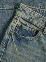 Jean wide fit de tiro medio, pierna curva y corte relajado, confeccionado en denim con lavado desgastado y costuras decorativas segmentadas.