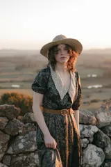 Vestido midi con estampado floral en tonos marrones y azules, cuello en V con detalle de puntilla blanca, mangas cortas abullonadas y cinturón marrón con hebilla dorada.