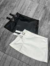 Minifalda negra de cuero sintético con hebillas plateadas.