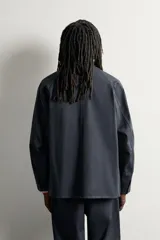 Sobrecamisa de algodón de corte relajado, color negro con efecto gastado, cuello con solapas de muesca, mangas largas raglán y cierre frontal con botones. Cuenta con bolsillos frontales de plastrón en el pecho y en la parte inferior.