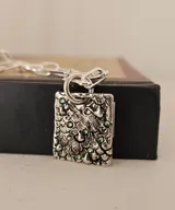 Collar de plata con medalla rectangular texturizada e incrustaciones de cristales verdes, suspendido de una cadena de eslabones.