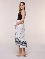 Vestido midi combinado de corte fluido. Presenta un torso ajustado acanalado sin mangas, con cuello redondo y sisas clásicas. Cuenta con cintura elastizada con lazo para anudar y falda evasé con estampado floral y geométrico, finalizando con un volante en el ruedo.