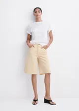 Bermuda de denim color amarillo pastel, de tiro bajo, corte recto y diseño de cinco bolsillos con cierre de botón y cremallera, y terminaciones deshilachadas.