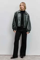 Cazadora de estilo bomber confeccionada en material efecto piel color verde oscuro. Presenta cuello camisero, cierre frontal con cremallera, mangas largas abullonadas con puños elásticos y un corte ligeramente cropped.