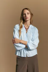 Camisa de manga larga color blanco, con cuello mao y escote en V. Presenta frunces en el canesú, cierre frontal con botones y mangas amplias con puños abotonados.