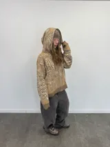 Buzo tipo hoodie con cierre frontal completo, confeccionado en tejido de punto grueso de algodón con diseño gráfico abstracto y tipográfico. Presenta capucha con bordado, puños y ruedo acanalados, y etiqueta de marca en la manga.