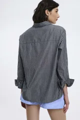 Camisa popelina rayada color rojo y blanco, con corte oversized, abotonadura frontal y en las mangas, y un bolsillo frontal.