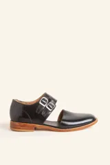 Zapato de cuero negro tipo monk strap con aberturas laterales y doble hebilla metálica. Presenta una suela de cuero con taco bajo de madera.