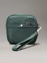 Riñonera verde militar de poliéster reciclado, con correa ajustable con clip, cierre de cremallera, dos bolsillos exteriores con anillas en D y logo de Calvin Klein en el frente. Se pliega y se cierra con cremallera para crear una cartera de muñeca.
