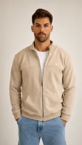 Campera de algodón color beige, con cierre frontal completo, cuello alto, bolsillos tipo canguro y puños y ruedo acanalados. Presenta un pequeño logo bordado en el pecho.