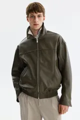 Campera verde militar de tejido revestido con cuello alto, cierre frontal de cremallera metálica, bolsillos laterales y elástico fruncido en el bajo y los puños.