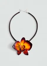Collar con cordón oscuro y colgante central en forma de orquídea con acabado esmaltado en tonos degradados de naranja, amarillo y bordó.