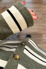 Cárdigan tejido a rayas horizontales en tonos verde militar, blanco y negro, con cuello en V y cierre frontal con botones marrones.