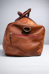 Bolso de viaje tipo weekender de cuero color tostado con asas y detalles en marrón oscuro, herrajes metálicos y bolsillo frontal con cierre.