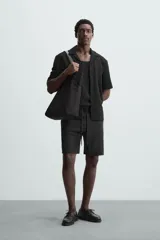 Camisa de corte regular fit confeccionada en tejido con estructura de color negro. Cuenta con cuello bowling, manga corta, aberturas laterales en el bajo y cierre frontal de botones.